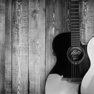 Two Acoustic Guitars In Black And White Against A Textured Wooden Wall Background.