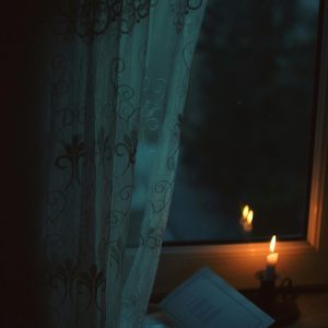 A Peaceful Scene With Candlelight Illuminating A Book By A Window At Night.
