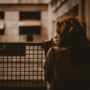A Woman Stands Alone Looking Through A Railing With A Sepia Toned, Contemplative Mood.