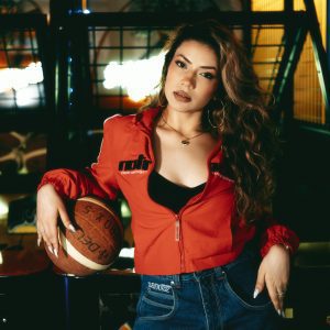 Confident Woman In Casual Outfit Posing With Basketball Indoors Under Neon Lights.