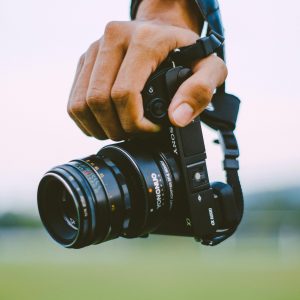 Close Up Of A Hand Holding A Vintage Camera Outdoors With A Blurred Green Background, Creating A Bokeh Effect.