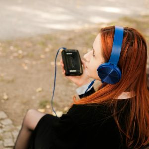 A Redheaded Teenager Listens To Music On Headphones While Sitting On A Bench Outside.