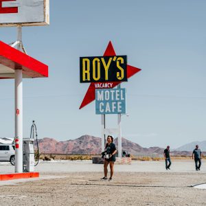 A Bright Gas Station And Motel With A Desert Backdrop, Featuring People And Vibrant Signage.