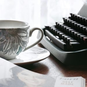A Nostalgic Desk Scene With A Typewriter And Floral Teacup, Evoking Retro Vibes.