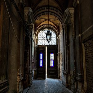 Gothic Style Corridor With Intricate Arches And A Stained Glass Door, Evoking Historic Architecture.