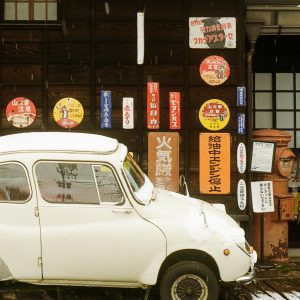A Classic White Car Parked Outside A Nostalgic Japanese Shop, Adorned With Vintage Signage.