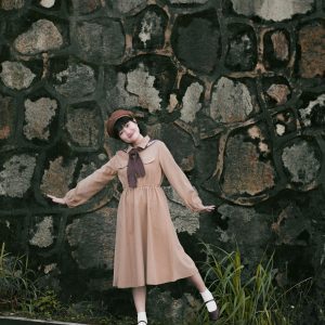 Elegant Woman In Vintage Attire Poses Playfully By A Rustic Stone Wall.