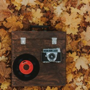 A Vintage Camera And Vinyl Record On A Wooden Box Surrounded By Autumn Leaves.