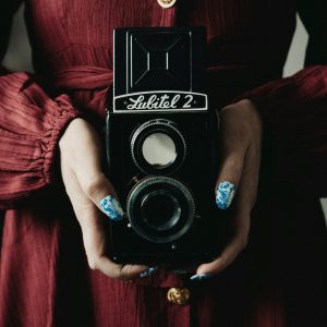 A Woman Wearing A Red Dress Holds A Vintage Lubitel 2 Camera, Emphasizing A Retro Aesthetic.