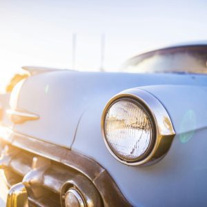 A Vibrant Close Up Of A Vintage Car's Headlight With Sun Flare Highlighting Its Classic Design.