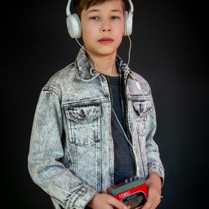 A Young Boy Wearing Headphones And Holding A Retro Walkman Against A Black Background.