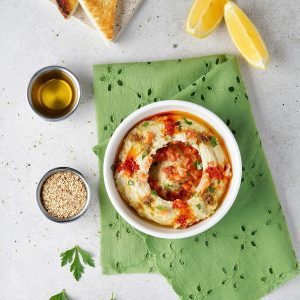 Appetizing Hummus Dish With Garnishes, Toast, And Sesame Seeds In A Bright, Inviting Setting.