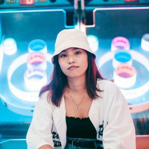 A Young Woman In Casual Fashion Sitting Near Arcade Games, Surrounded By Vibrant Neon Lights.