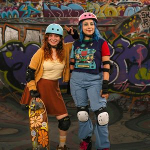 Two Female Skaters Stand At A Graffiti Covered Skatepark, Embracing Skate Culture.
