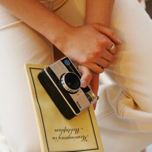 Close Up Of Hands Holding A Vintage Camera And Book Indoors, Evoking Nostalgia.