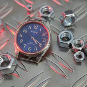 A Vintage Wristwatch And Metal Nuts On Textured Surface With Red Lighting Accents.