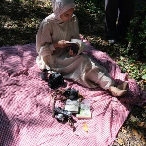 A Young Woman Enjoys A Peaceful Day Outdoors, Reading On A Picnic Blanket Surrounded By Vintage Cameras.