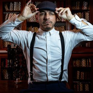 A Man In Vintage Attire Adjusts His Cap, Set In A Classic Buenos Aires Library.