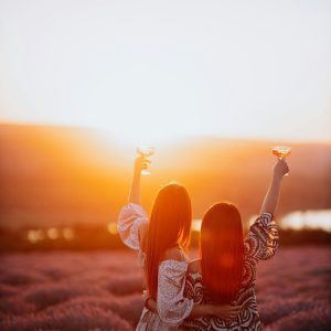 Two Women Enjoying A Sunset With Raised Glasses In A Lavender Field, Creating A Warm And Joyful Atmosphere.