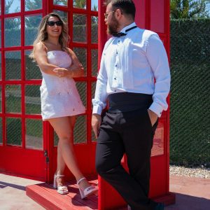 Stylish Couple In Formal Attire By A Red Telephone Box On A Sunny Day.