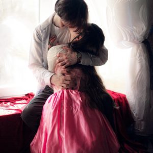 A Couple Embraces Tenderly In Front Of A Sunlit Window, Creating A Warm And Intimate Atmosphere.