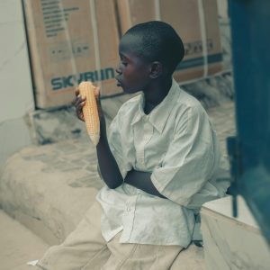 Boy Sitting On Steps Eating Corn, Urban Background, Relaxed Atmosphere.