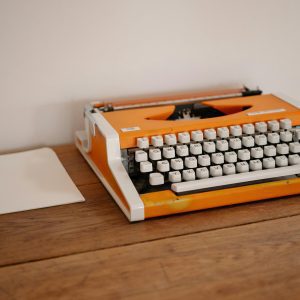 Retro Orange Typewriter On A Wooden Desk With A Blank Sheet Of Paper, Perfect For Nostalgic And Creative Concepts.