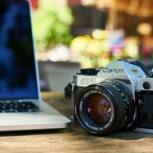 A Classic Canon Film Camera Beside A Laptop On A Wooden Table Outdoors.