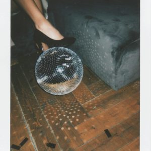 A Stylish Party Scene Featuring Black Heels And A Reflective Disco Ball On A Parquet Floor.
