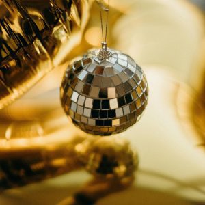 Shimmering Disco Ball Held Against A Warm Gold Reflective Background, Creating A Festive Atmosphere.
