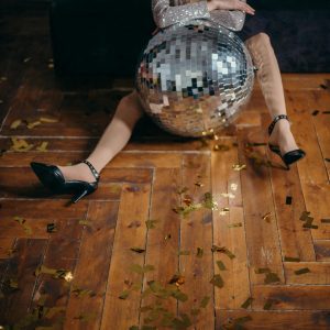 A Fashionable Woman Sitting With A Disco Ball Amid Scattered Confetti Indoors, Exuding Style And Celebration.