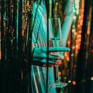 A Stylish Hand Holds A Champagne Glass Amidst A Glittering Party Backdrop, Exuding Celebration Vibes.