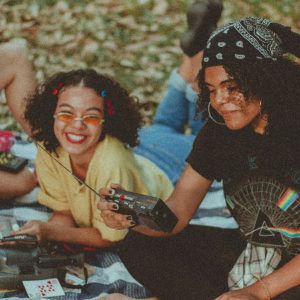 Three Women Having Fun With A Vintage Radio At An Outdoor Picnic, Embodying Retro Style And Cheerful Friendship.