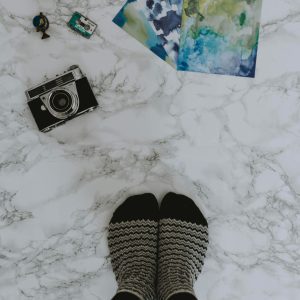 Top View Of Vintage Camera, Art Prints, Toy Car, And Feet With Socks On Marble Surface.
