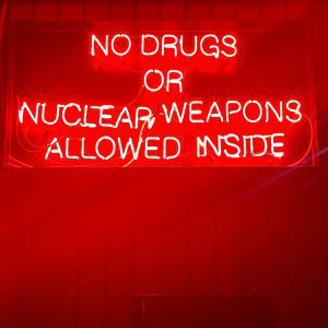 Bright Neon Sign Reading 'No Drugs Or Nuclear Weapons Allowed Inside' In A Bar Setting.