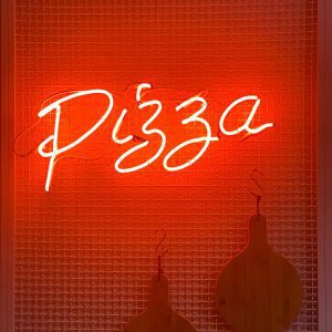 A Glowing Neon Sign Displaying The Word 'Pizza' On A Textured Red Background.