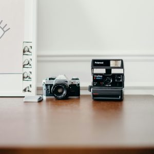 A Classic Polaroid OneStep And Vintage Film Camera On A Wooden Table With A Photo Frame.