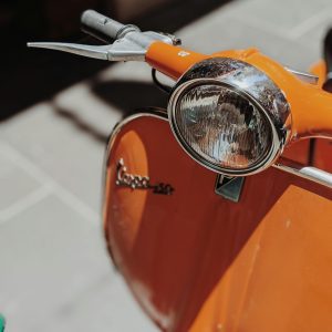 Close Up Of A Vintage Orange Vespa Scooter Parked Outdoors, Showcasing Its Classic Design.