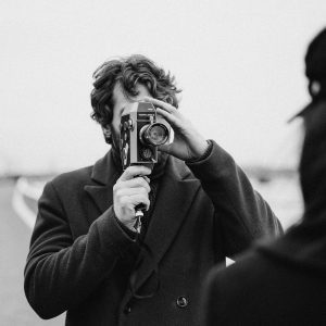 Monochrome Image Of A Man With An Old Camera Capturing A Scene Outdoors.