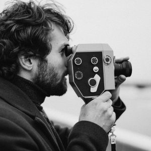 Side View Of A Man Filming With A Vintage Camera In A Black And White Setting.