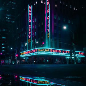 Vibrant Nighttime View Of Radio City Music Hall With Neon Lights And Reflections.