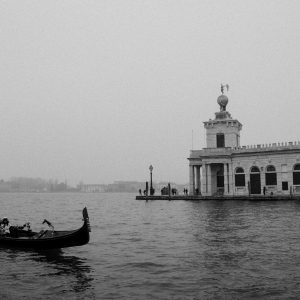 Black And White Photo Of A Gondola On A Foggy Canal In Venice, Italy, With Historic Architecture.