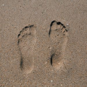 Close Up Of Two Footprints In Sand, Evoking Summer Beach Vibes.
