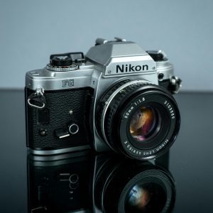 Close Up Of A Classic Nikon Film Camera With Chrome Details Reflected On A Surface.