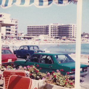 A Nostalgic Summer Beach View With Vintage Cars Parked Along A Seaside Road.