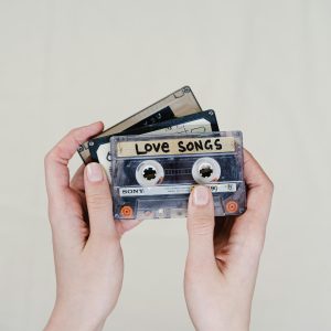 Hands Holding Cassette Tapes Labeled 'Love Songs', Highlighting 90s Nostalgia.