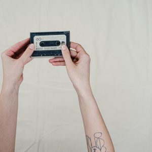 Hands Holding A Retro Cassette Tape Against A Plain Background, Evoking Nostalgia.