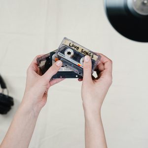 Hands Holding Love Songs Cassette Tapes Over Vinyl, Showcasing Nostalgic 90s Music Culture.