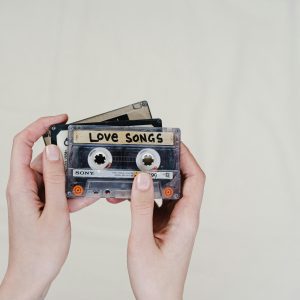 Hands Holding Vintage Cassette Tapes, Including A 'Love Songs' Label, Evoking Nostalgia.