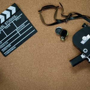 Flat Lay Of Vintage Cinema Equipment With A Film Slate And Camera On A Cork Board Background.